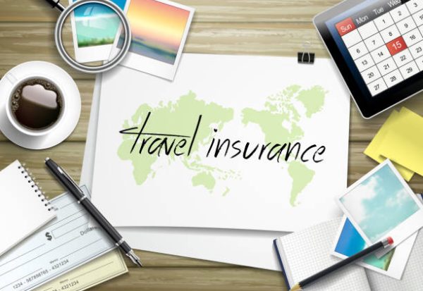 top view of travel items on wooden table with travel insurance written on paper